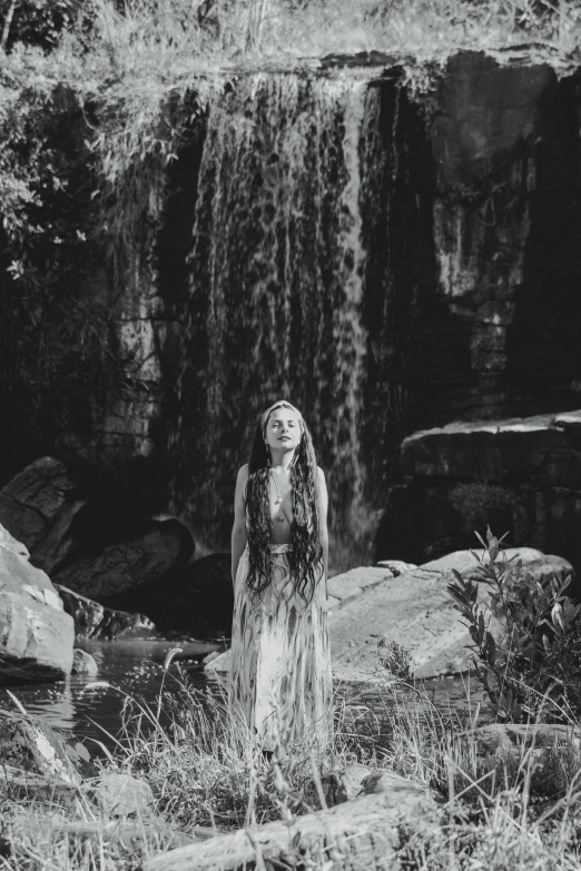 a woman standing in front of a waterfall, a black and white photo, inspired by Nell Dorr, renaissance, movie still of the alien girl, florence pugh, performing a music video, southern gothic