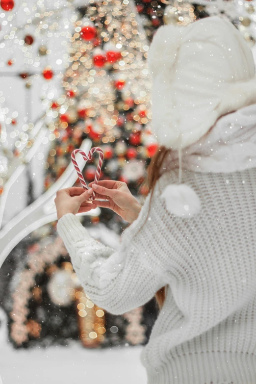 a woman holding a candy cane in front of a christmas tree, a picture, by Julia Pishtar, trending on pexels, hearts, winter wonderland, white trendy clothes, carousel