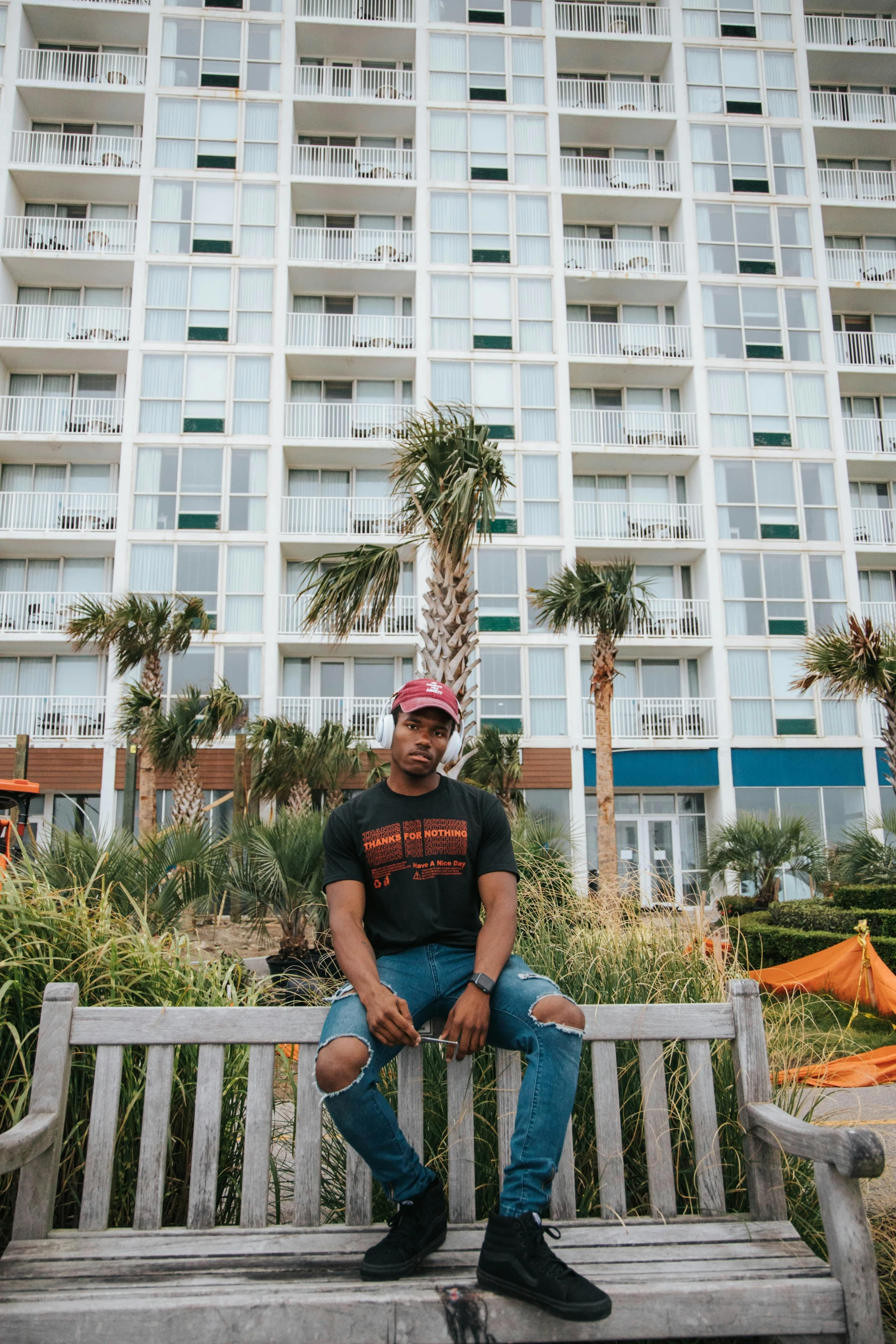 a man sitting on a bench in front of a building, posing on a beach with the ocean, hotel room, kendrick lamar, african canadian