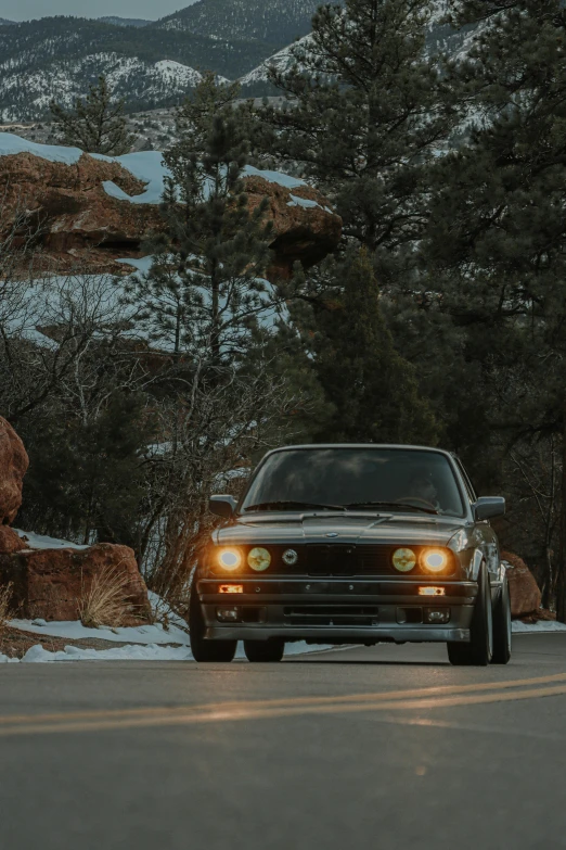 a car driving down a road with mountains in the background, by Drew Tucker, unsplash contest winner, renaissance, bmw e 3 0, custom headlights, profile image, with a tree in the background