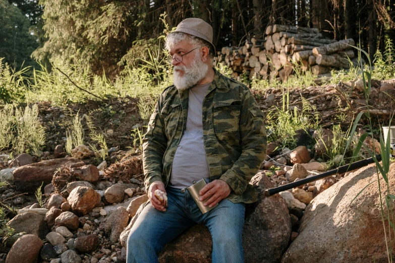 a man sitting on top of a pile of rocks, overalls and a white beard, grandfatherly, wearing camo, forest picnic