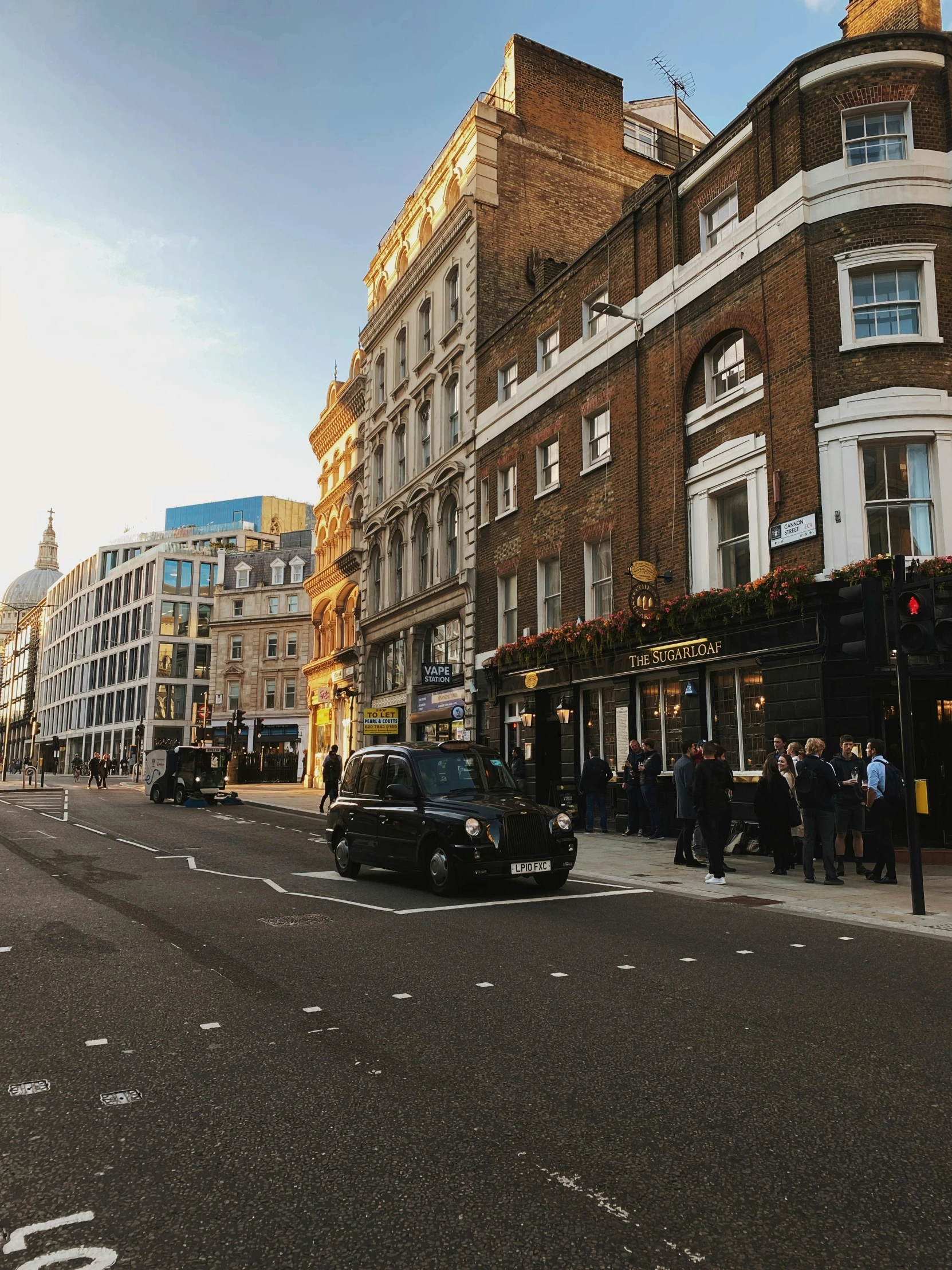 a car driving down a street next to tall buildings, a photo, london streets in background, crowded inn in the background, background image, uncropped