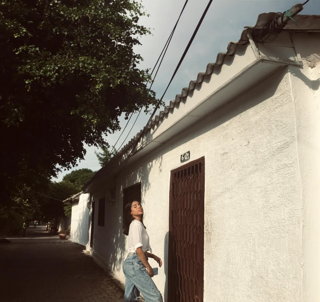 a woman standing in front of a white building, a picture, shady alleys, background image, gongbi, at home