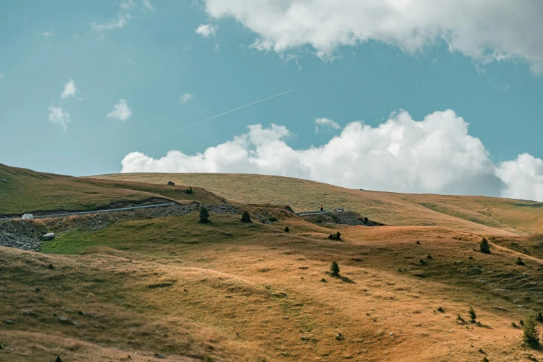 a man flying a kite on top of a lush green hillside, les nabis, minimalist photo, brown, scattered clouds, unsplash 4k