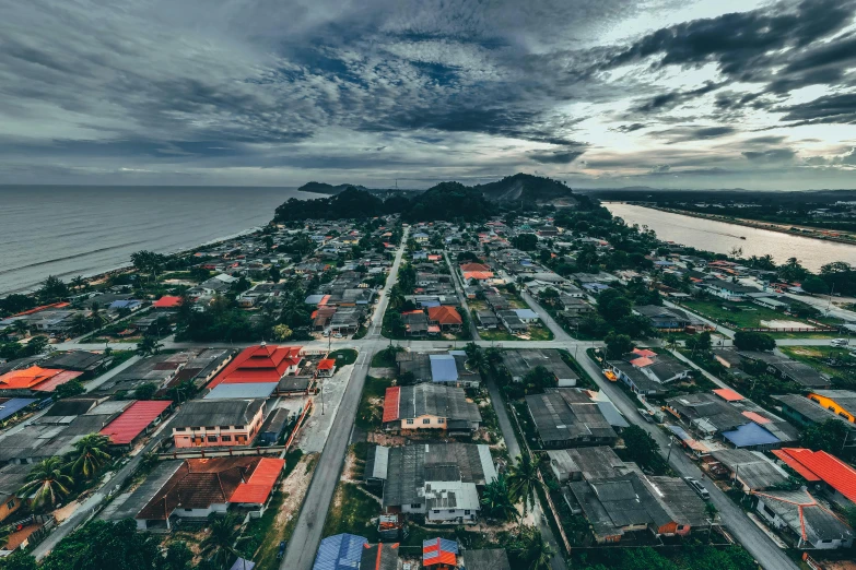 a city next to the ocean under a cloudy sky, unsplash contest winner, sumatraism, in a suburb, drone footage, thumbnail, looking partly to the left