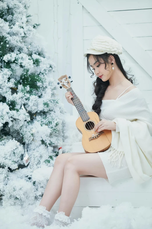 a woman sitting in front of a christmas tree playing a guitar, an album cover, inspired by Song Xu, pexels contest winner, romanticism, ulzzang, white snow, ukulele, dressed in white