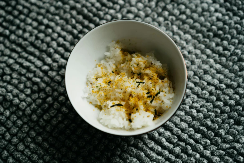 a close up of a bowl of food on a table, a picture, unsplash, sōsaku hanga, scattered golden flakes, rice, with lemon skin texture, thumbnail