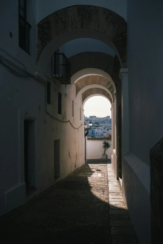 a narrow alley with a light at the end, unsplash contest winner, neoclassicism, ibiza, low quality photo, white sweeping arches, city view