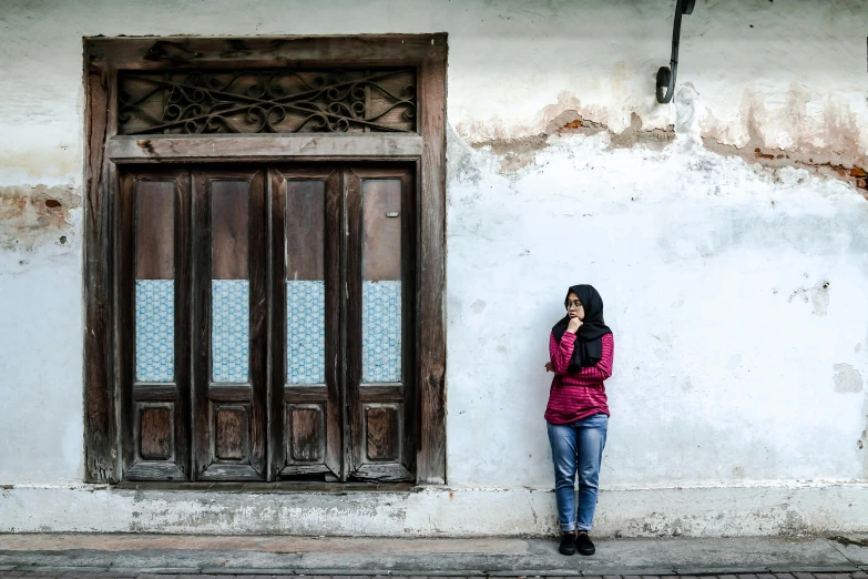 a woman standing in front of a building talking on a cell phone, a picture, inspired by Steve McCurry, pexels contest winner, hyperrealism, islamic, a wooden, an abandoned old, malaysian