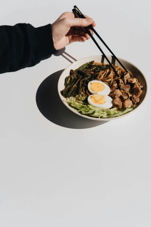 a person holding chopsticks over a bowl of food, on a white table, ignant, no background and shadows, 6 : 3 0 am