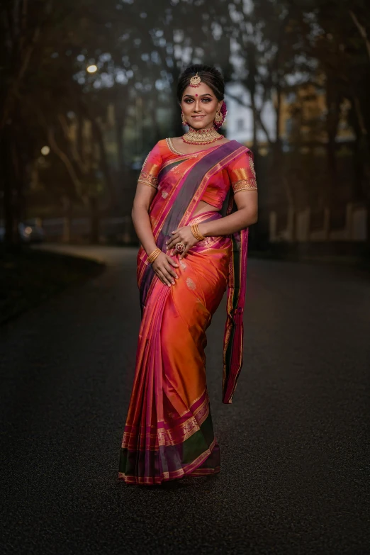 a woman in a sari standing in the middle of a road, inspired by T. K. Padmini, pexels contest winner, light red and orange mood, square, dressed in colorful silk, elegant glamor pose