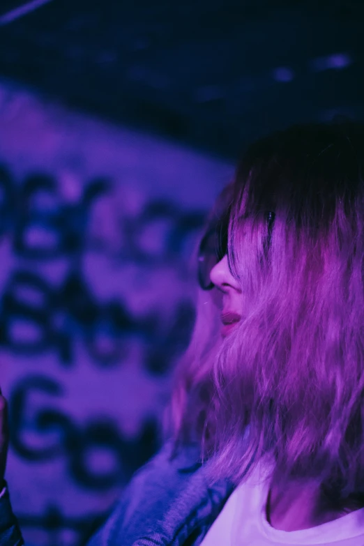 a woman holding a cell phone up to her ear, an album cover, inspired by Elsa Bleda, unsplash, happening, purple long hair, performance, neon basement, grainy footage