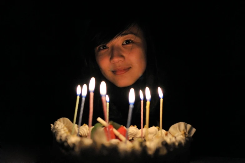a woman standing in front of a cake with lit candles, by Maki Haku, pexels, hyperrealism, bjork smiling, taken in the late 2010s, she is about 1 6 years old, dark vignette