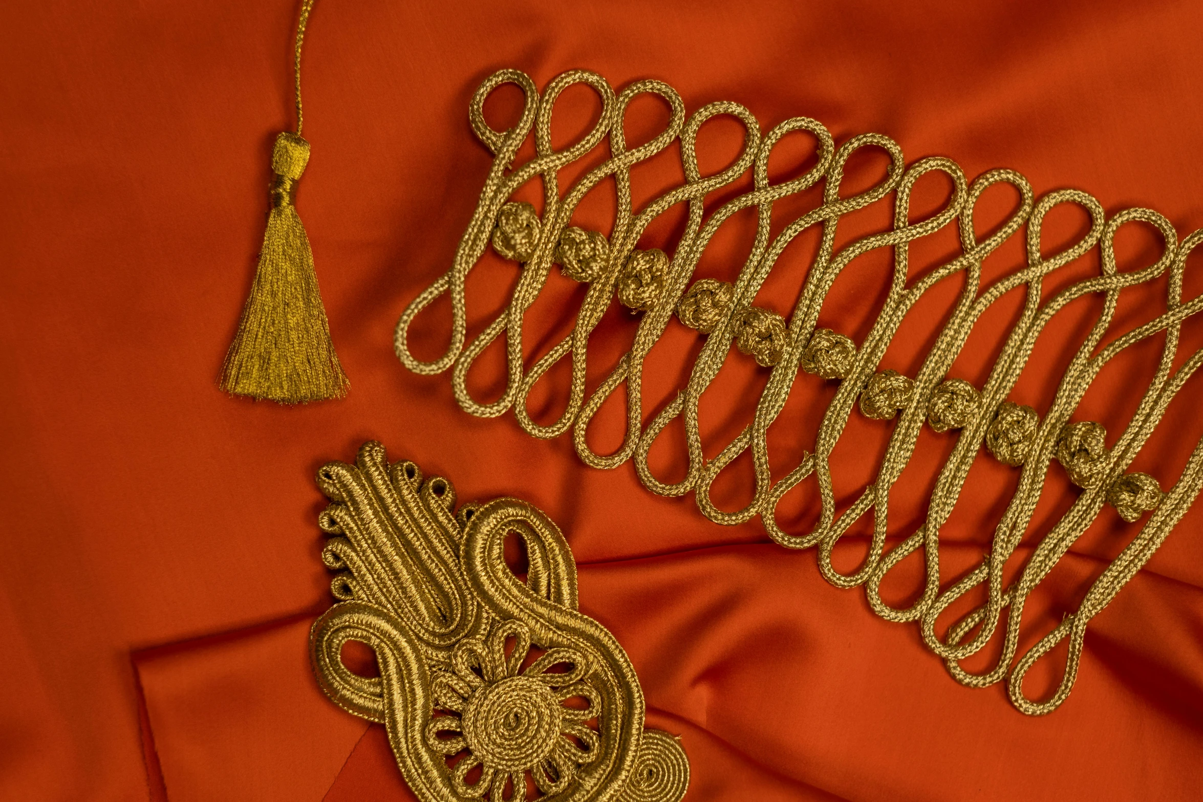 a close up of a piece of clothing with a tassel, an album cover, arabesque, golden accessories, webbing, sinuous, ochre