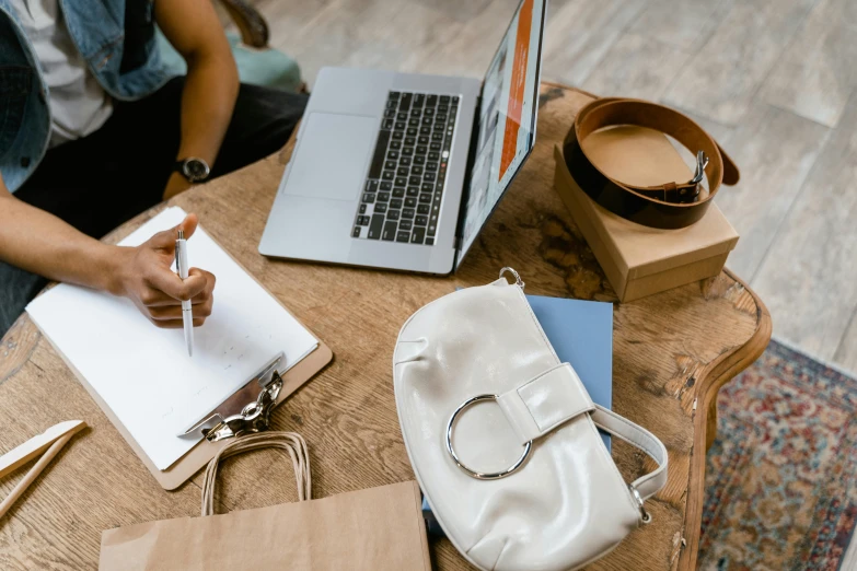 a person sitting at a table with a laptop and notebook, by Julia Pishtar, trending on pexels, bags, inspect in inventory image, thumbnail, background image