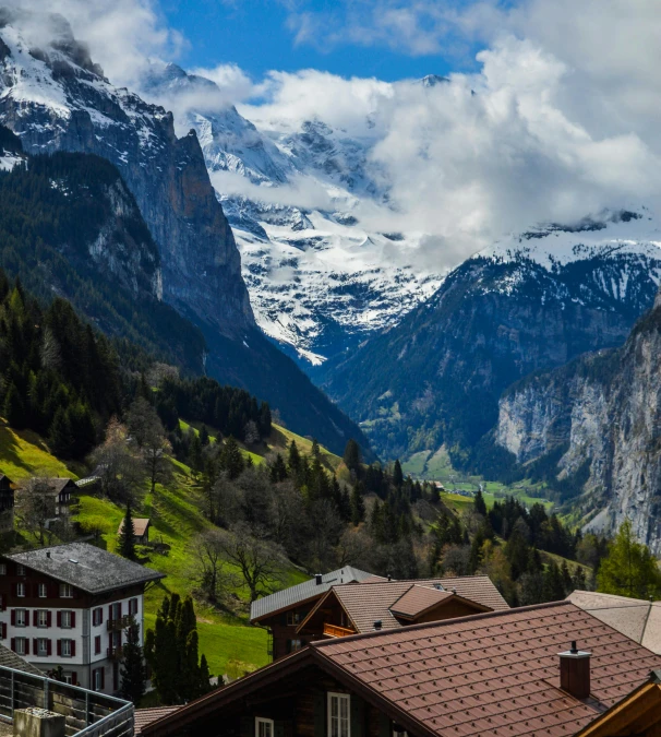 a group of houses sitting on top of a lush green hillside, by Sebastian Spreng, pexels contest winner, snow capped mountains, geiger, a wooden, overlooking