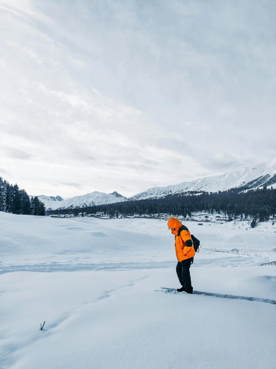 a person in an orange jacket standing in the snow, a photo, inspired by Werner Andermatt, pexels contest winner, hurufiyya, wide views, russia, grey, distant full body view