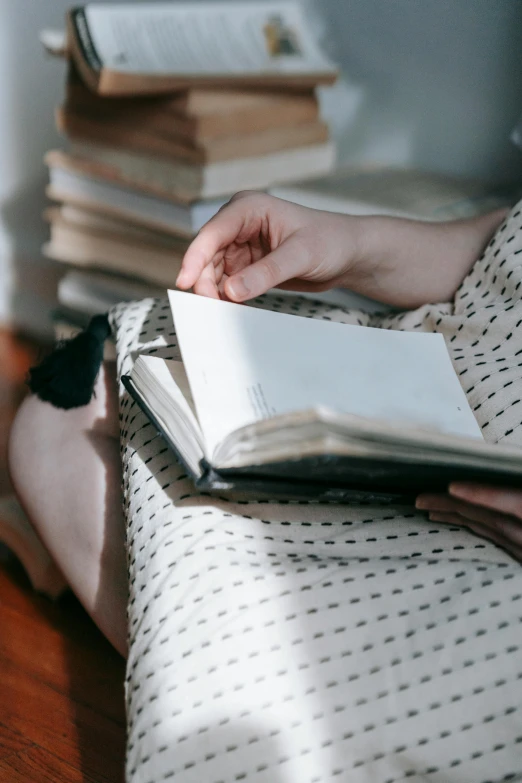 a woman sitting on a bed reading a book, pexels contest winner, white shirt and grey skirt, diary on her hand, uncropped, holding books