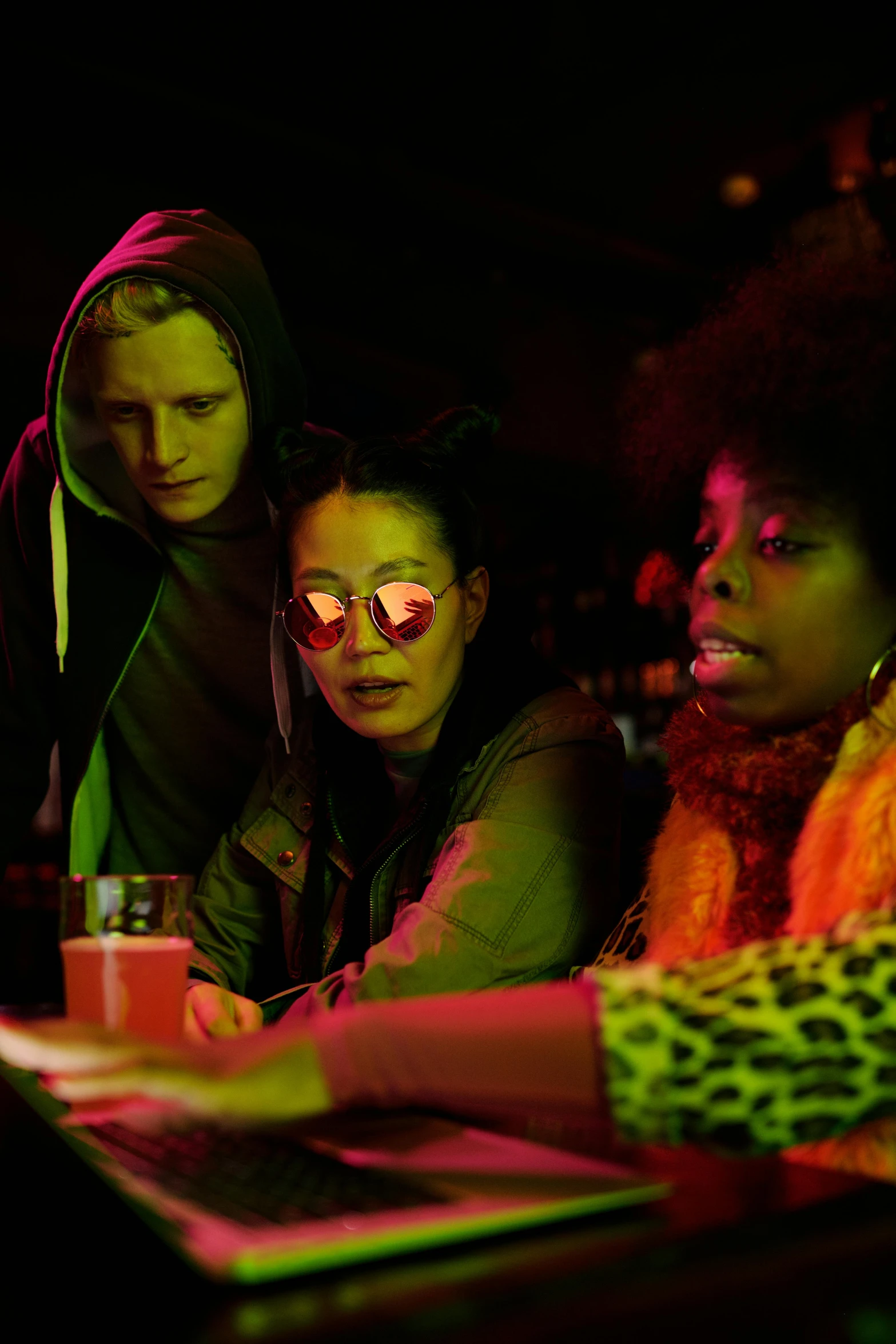 a group of people sitting around a laptop computer, by Jacob Toorenvliet, neon lenses, at netflix, drinking at the bar, wearing a scarlet hoodie