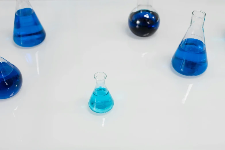 a group of glass flasks filled with blue liquid, trending on unsplash, analytical art, on a white table, cinematic shot ar 9:16 -n 6 -g, atoms floating, oil spill