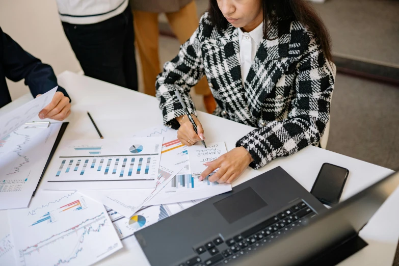 a woman sitting at a table with papers and a laptop, trending on pexels, analytical art, standing in class, graphs, nivanh chanthara, low quality photo