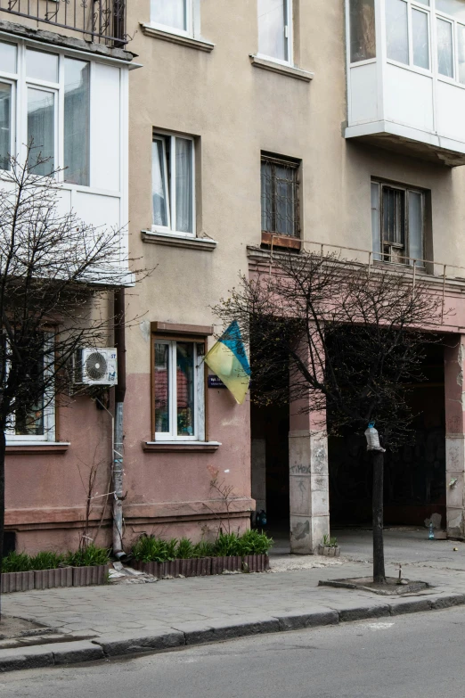 a man riding a motorcycle down a street next to tall buildings, an album cover, inspired by Viktor Madarász, socialist realism, ukrainian flag on the left side, in front of the house, photograph taken in 2 0 2 0, opposite the lift-shaft