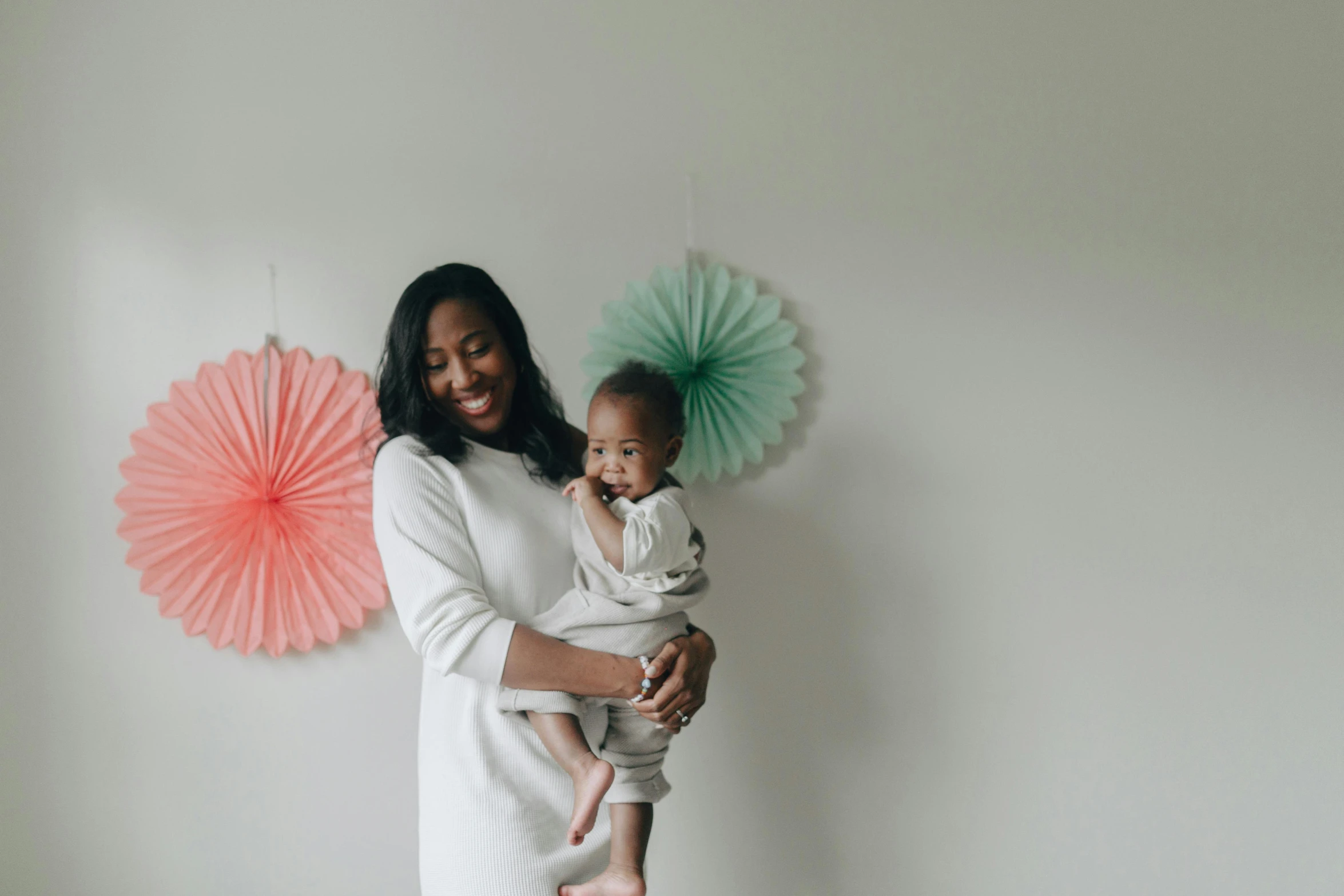 a woman holding a baby in her arms, a photo, by Arabella Rankin, pexels contest winner, in front of white back drop, diverse outfits, at home, celebrating