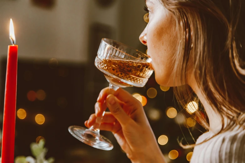 a woman holding a wine glass in front of a candle, pexels contest winner, drinking a martini, profile image, festive, close up shot from the side