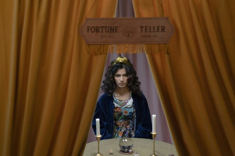 a woman sitting at a table in front of a sign, inspired by E. Charlton Fortune, pexels contest winner, magic realism, fortune teller, still image from tv series, morena baccarin, 1 7 th century duchess