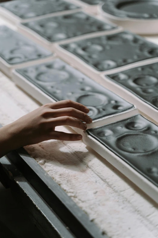 a person touching a piece of glass on a table, a silk screen, trending on unsplash, process art, made of cement and concrete, portholes, inspect in inventory image, plush leather pads