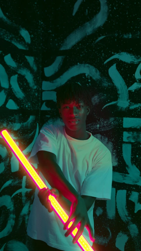 a man holding a neon light saber in front of a graffiti wall, an album cover, inspired by Liam Wong, unsplash, afrofuturism, 2 1 savage, color vhs picture quality, black teenage boy, colorized photon