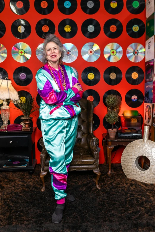 a woman standing in front of a wall covered in records, maximalism, wearing! robes!! of silver, betty white, neon colored suit, studio photo