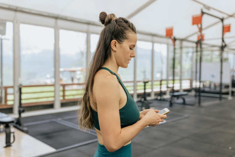 a woman standing in a gym holding a cell phone, by Emma Andijewska, pexels contest winner, happening, al fresco, avatar image, lachlan bailey, profile image