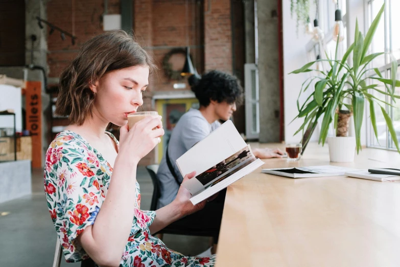 a woman sitting at a table reading a book, pexels contest winner, private press, medium shot of two characters, modern technology, small hipster coffee shop, avatar image