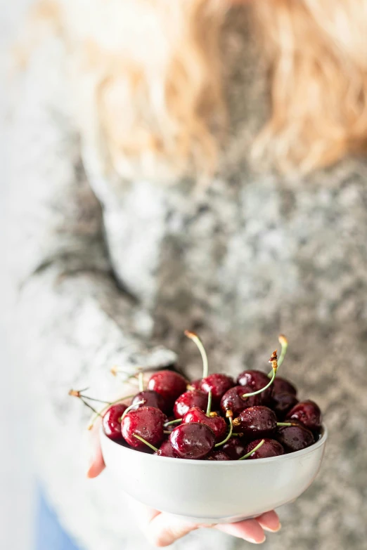 a woman holding a bowl of cherries, by Julia Pishtar, unsplash, fine art, perfect crisp light, winter, standing on a shelf, high quality product image”