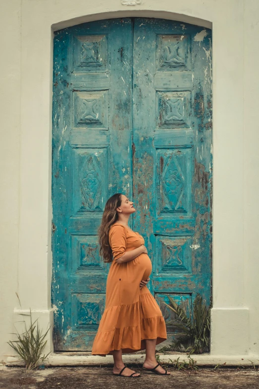 a pregnant woman standing in front of a blue door, by Sven Erixson, pexels contest winner, ocher and turquoise colors, doing a majestic pose, in front of white back drop, the birth