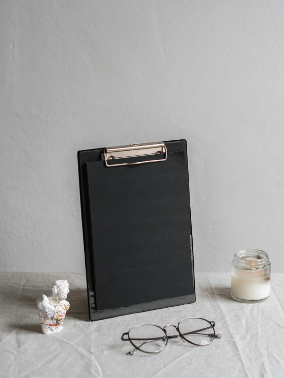 a clipboard sitting on top of a table next to a pair of glasses, black on black, full product shot, square, glazed