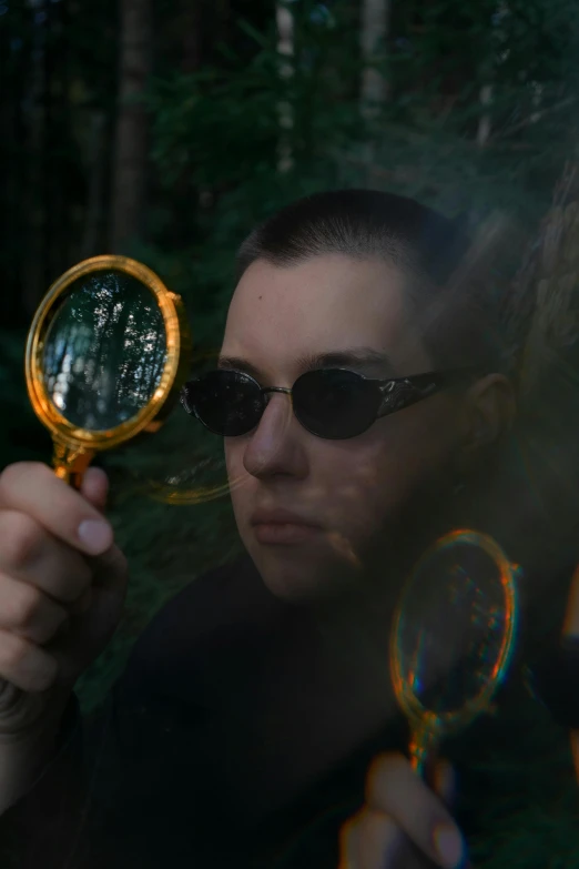 a woman holding a magnifying glass in front of her face, a picture, by Attila Meszlenyi, pexels contest winner, holography, yung lean, wearing gold glasses, julian ope, in forest