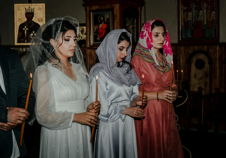 a group of people standing next to each other holding candles, a colorized photo, pexels, hurufiyya, wearing cross on robe, three women, wedding, middle eastern skin