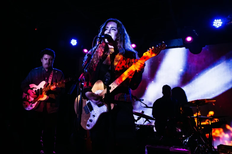 a woman that is playing a guitar on a stage, pexels, private press, 3 band lineup, brightly colored, full faces, 3 / 4 wide shot