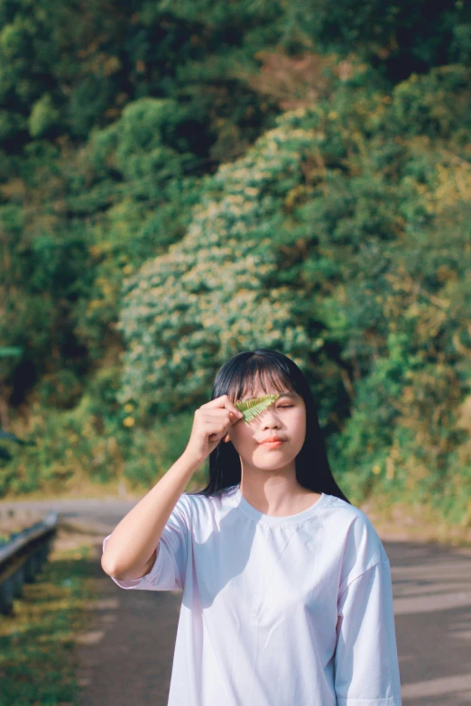 a woman standing on the side of a road, by Tan Ting-pho, pexels contest winner, light green tone beautiful face, greenery, hong june hyung, hand on cheek