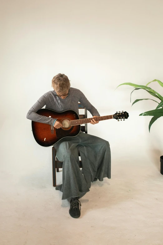 a man sitting in a chair playing a guitar, next to a plant, model photograph, grey, 155 cm tall