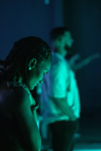 a couple of people that are standing in the dark, ambient teal light, figure meditating close shot, in profile, promo image