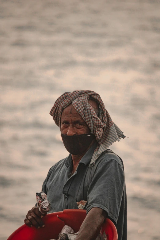 a man standing in front of a body of water, wearing bandit mask, faded and dusty, assamese aesthetic, wearing dark maritime clothing