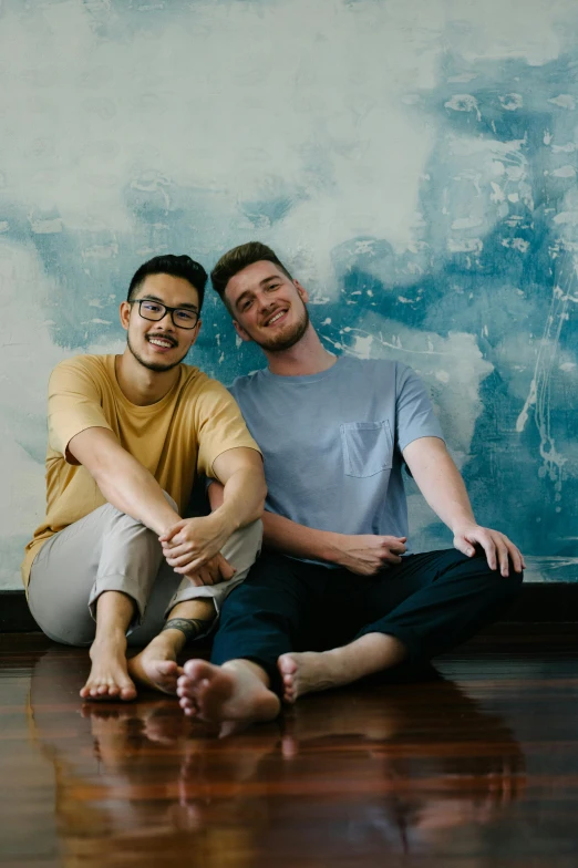 a couple of men sitting on top of a wooden floor, by Adam Dario Keel, slightly smiling, malaysian, two buddies sitting in a room, straya