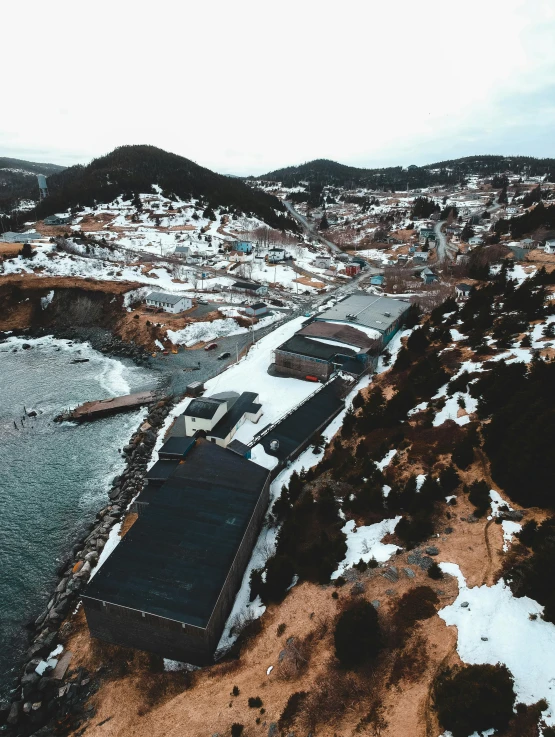 a beach covered in snow next to a body of water, by Kyle Lambert, pexels contest winner, renaissance, mining outpost, buildings covered in black tar, aerial footage, thumbnail