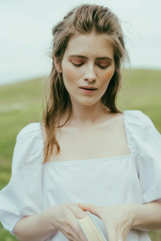 a woman standing in a field holding a book, inspired by Anita Malfatti, renaissance, white top, neck zoomed in from lips down, white summer dress, photoshoot for skincare brand