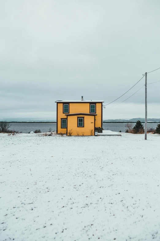 a yellow house sitting on top of a snow covered field, inspired by Wes Anderson, pexels contest winner, near the sea, gray skies, contrasting colors, francois legault