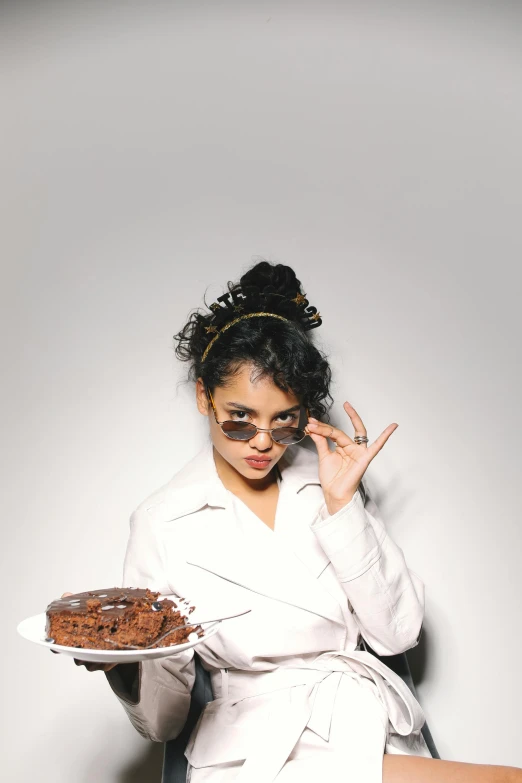 a woman sitting on a chair holding a plate of food, an album cover, inspired by Pia Fries, trending on pexels, the greatest cake, with sunglass, mixed race, hair bun