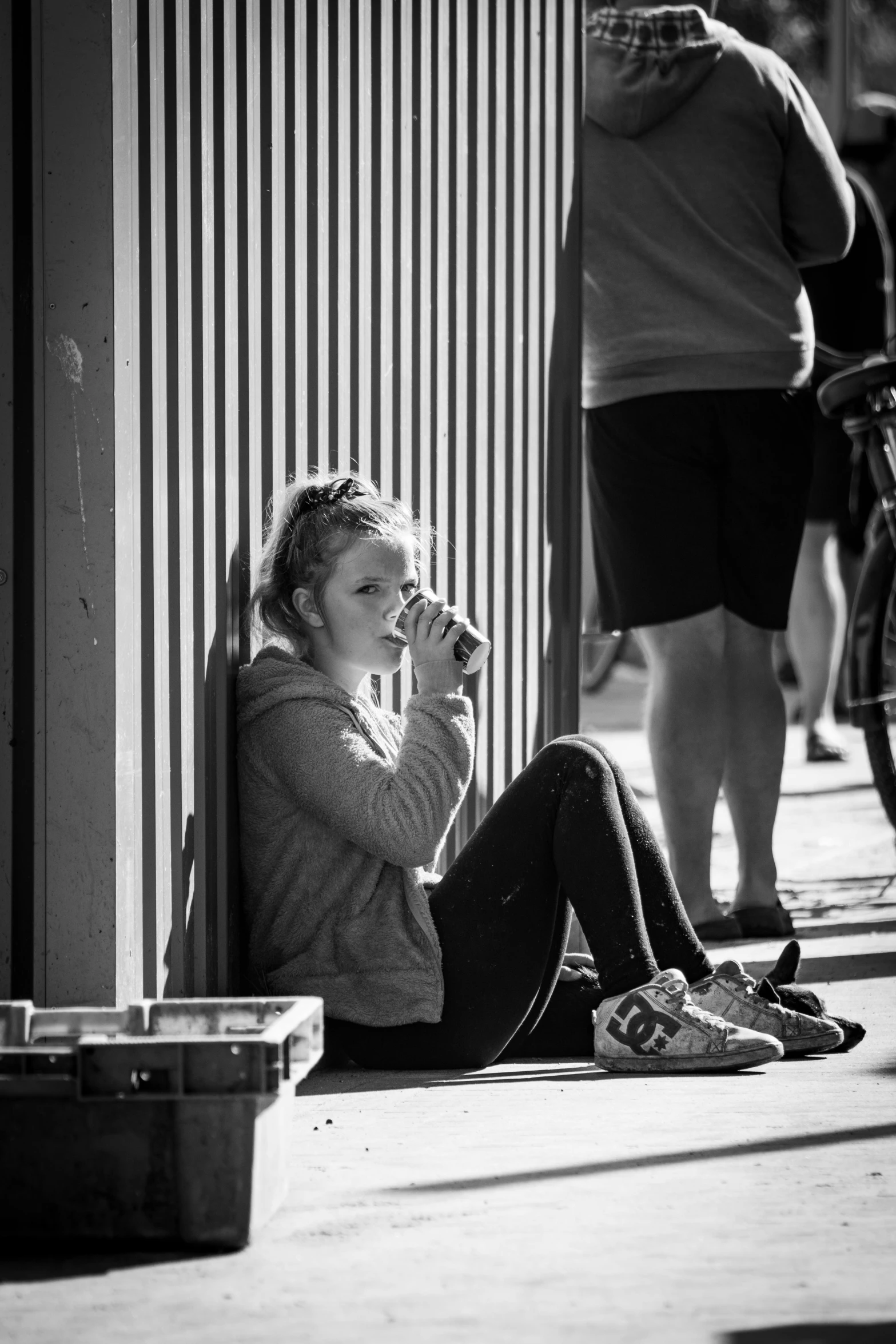 a woman sitting on the sidewalk talking on a cell phone, a black and white photo, by Lee Loughridge, pexels contest winner, realism, athlete photography, warm sunshine, tired and drunk, eating